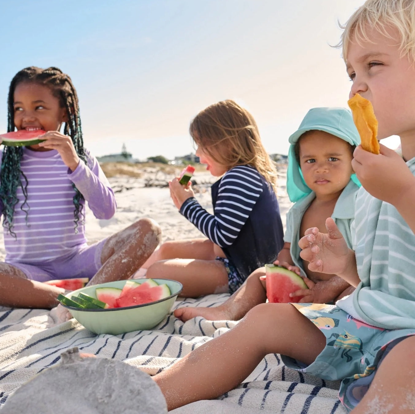 Group of kids in sustainable sun-protective clothing eating snacks by the ocean