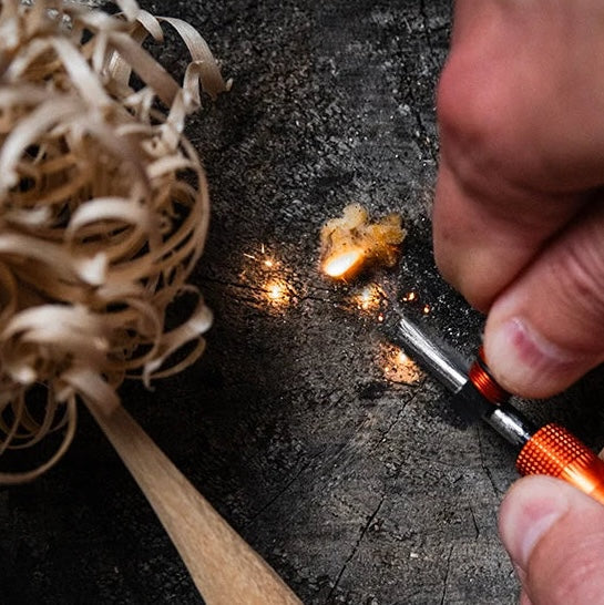 Essential camping gear — fire starter tool creating sparks on a wooden surface.