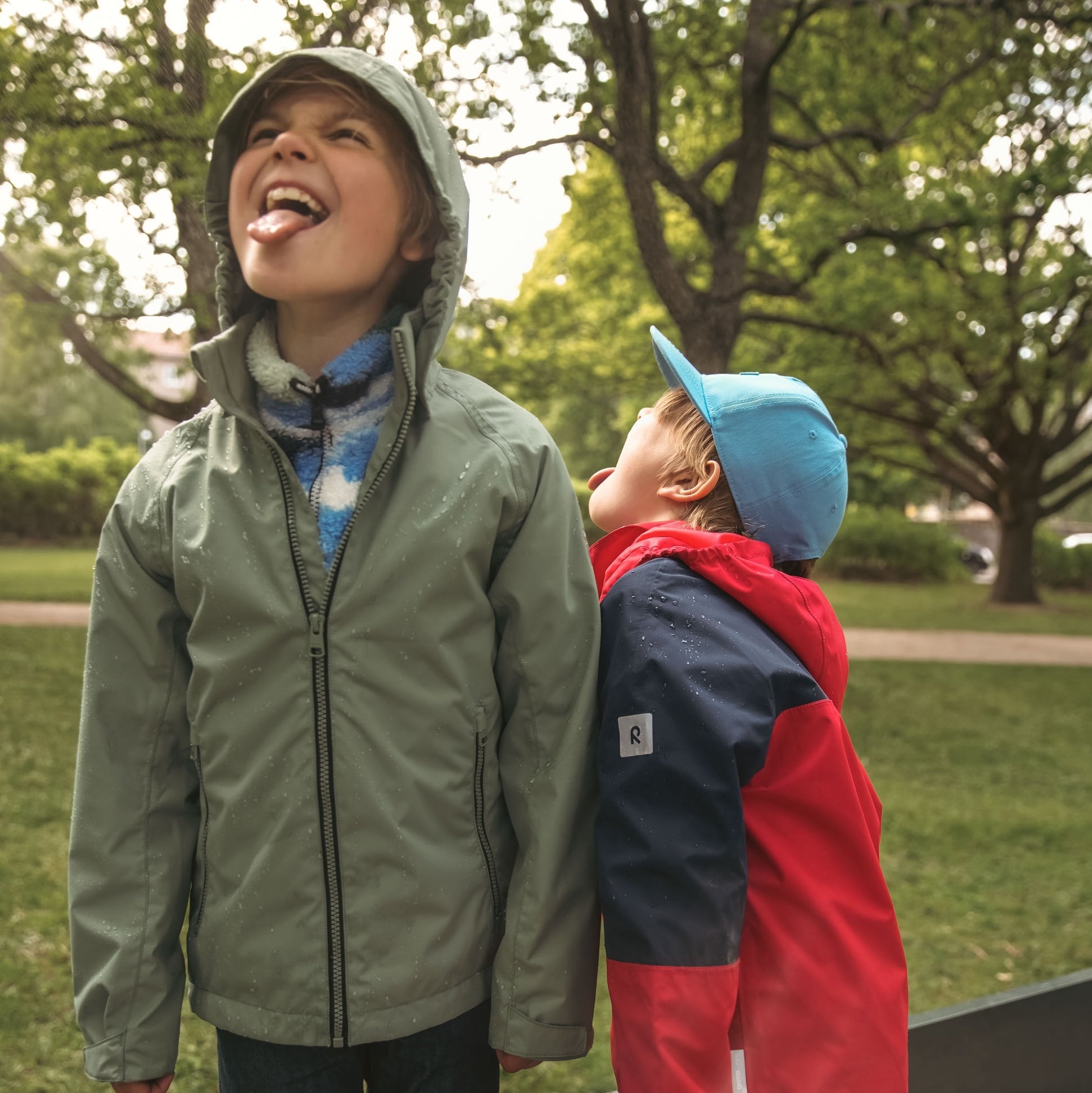 Child splashing in shallow water wearing waterproof green rain gear — celebrating outdoor play in wet autumn weather