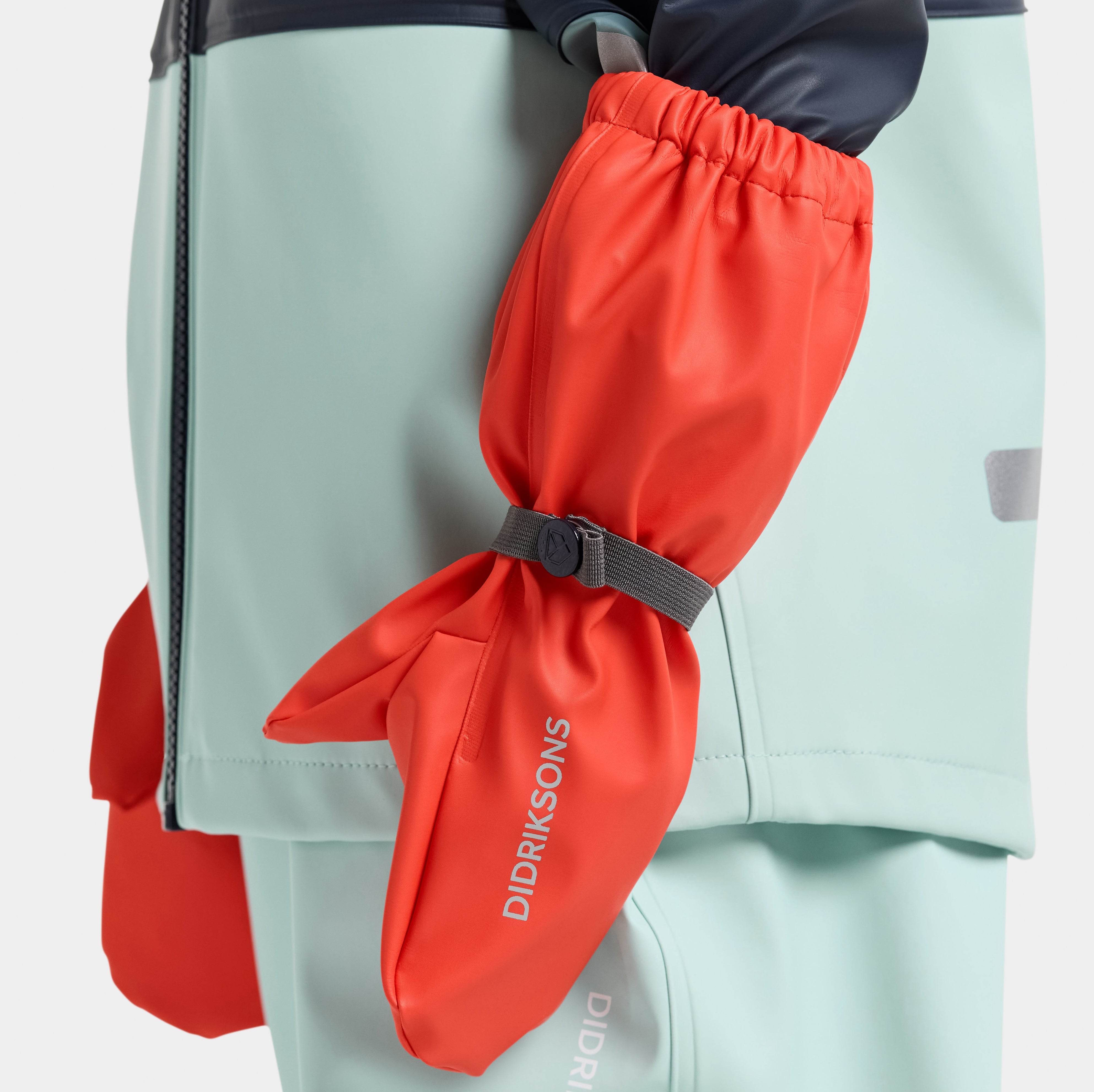 Child wearing green waterproof rain pants and mittens splashing in puddles — durable outdoor rain gear for kids.