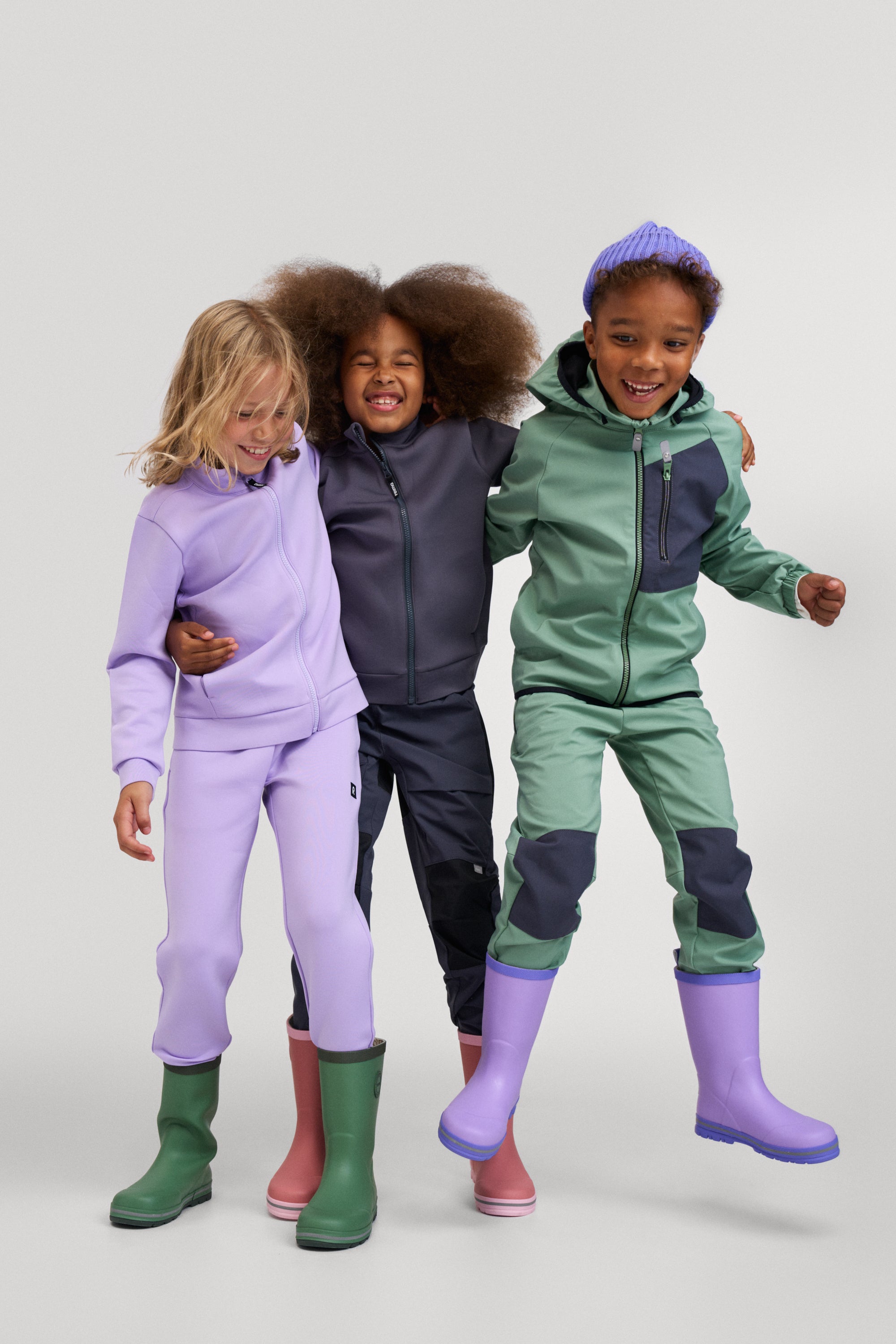 Three children wearing colorful outfits with matching rain boots on a white background