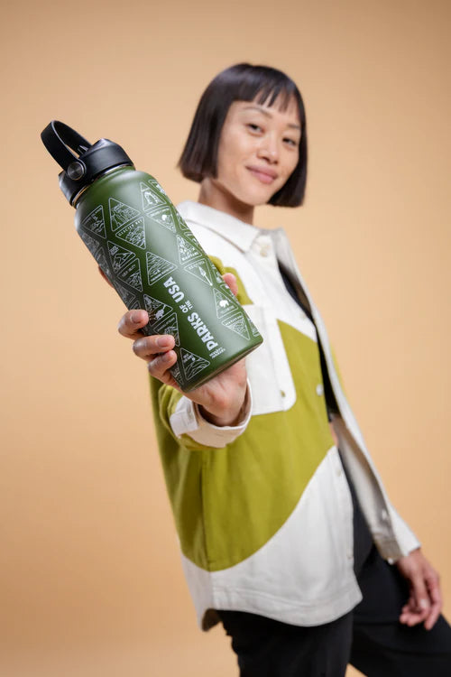 Person holding a green water bottle with a pattern against a beige background