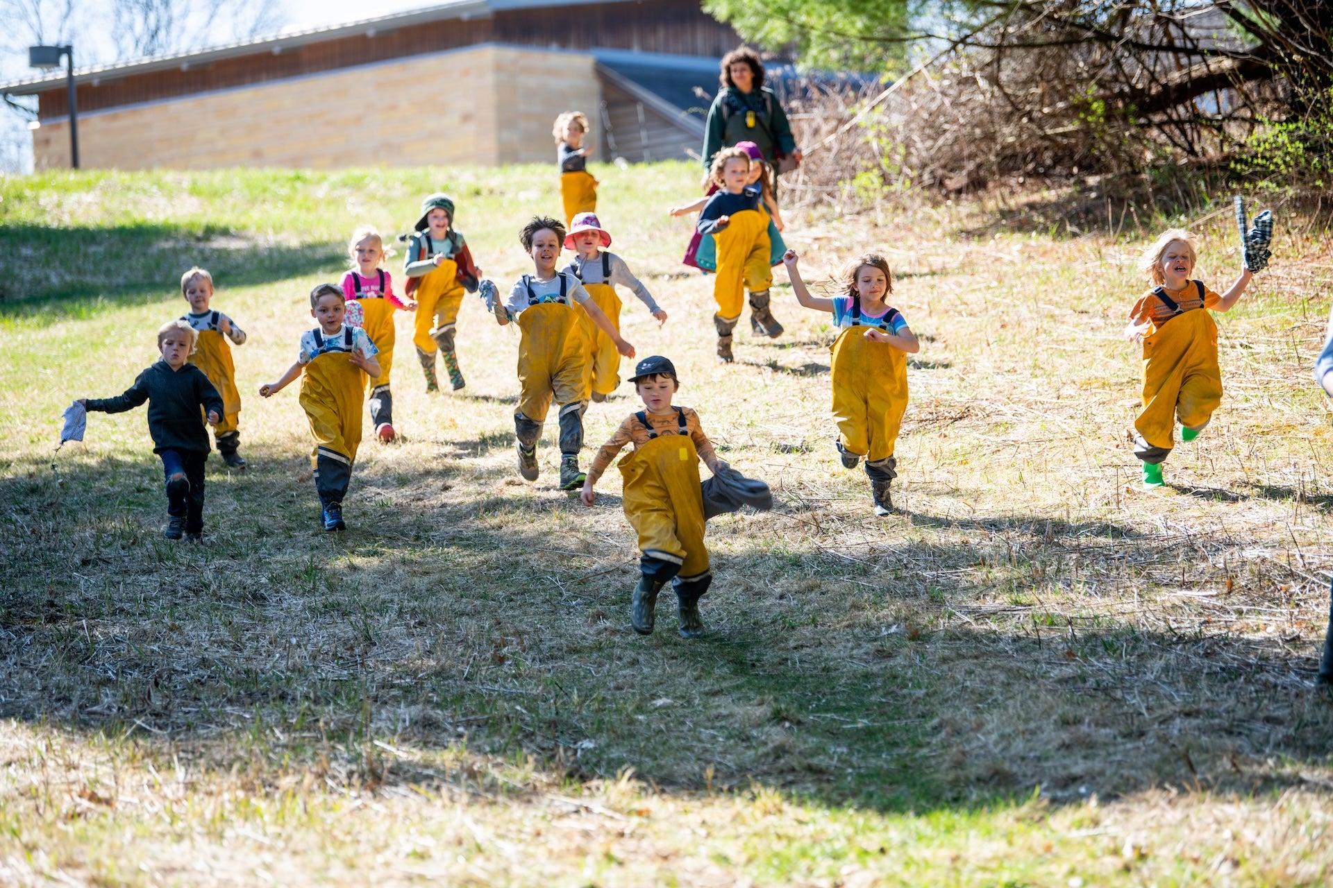 Children in yellow raincoats and boots running outdoors on a grassy area.