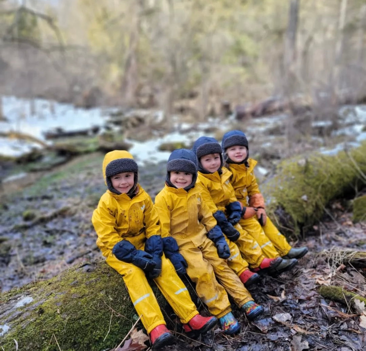 Children in yellow raincoats sitting on a log in a forest setting