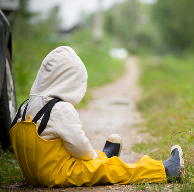 Person in a yellow raincoat and white hood sitting on a path in a natural setting