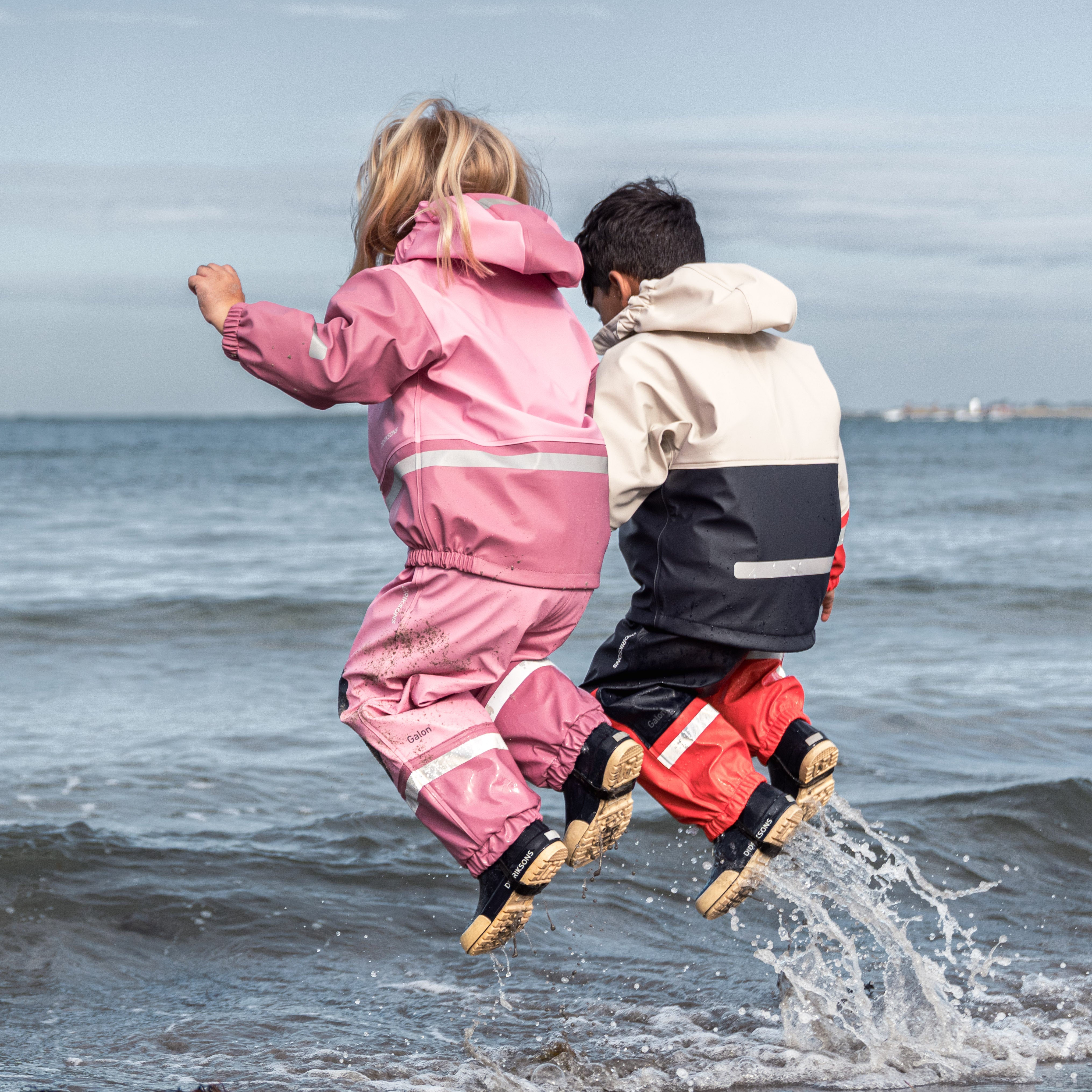 Child exploring coastal rocks in waterproof outdoor rain gear and fleece jacket — durable kids’ adventure clothing for spring and fall weather.
