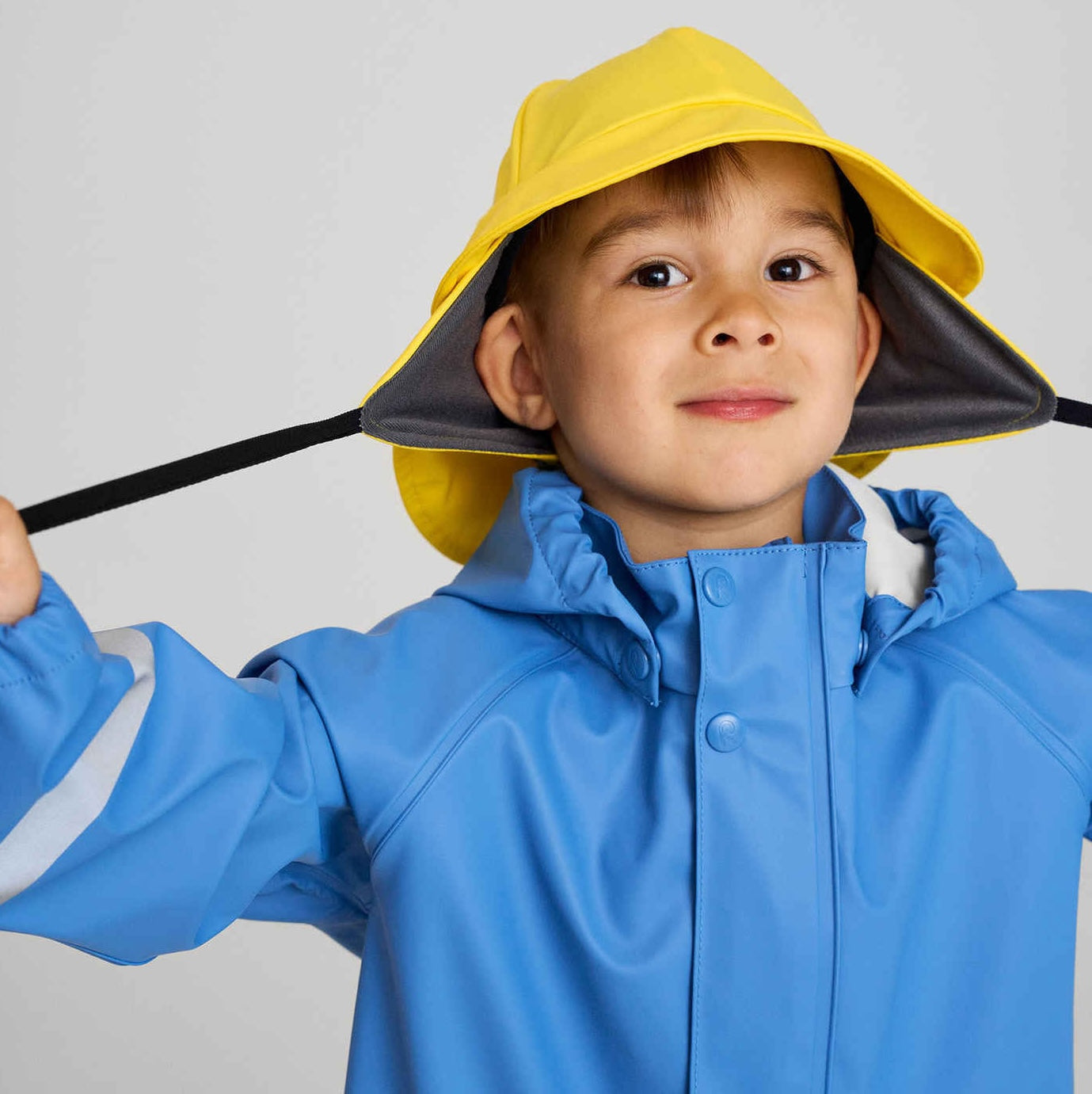 Smiling child in pink waterproof rain jacket and matching hat — cheerful kids outerwear for spring and autumn adventures.