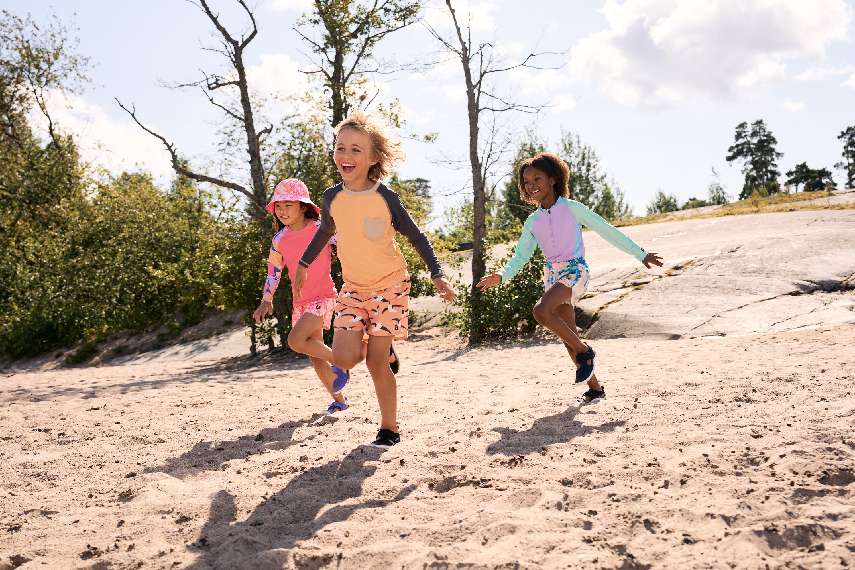 Three children running on a sandy path with trees in the background for Outdoor School Shop.  